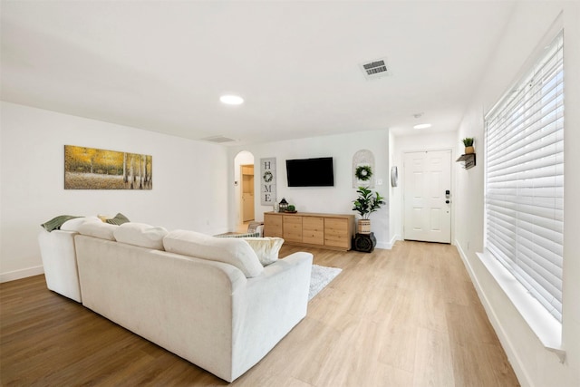 living room featuring visible vents, arched walkways, baseboards, and light wood-style flooring