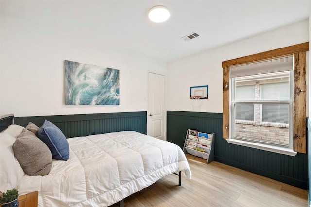 bedroom featuring light wood-style floors, visible vents, and wainscoting