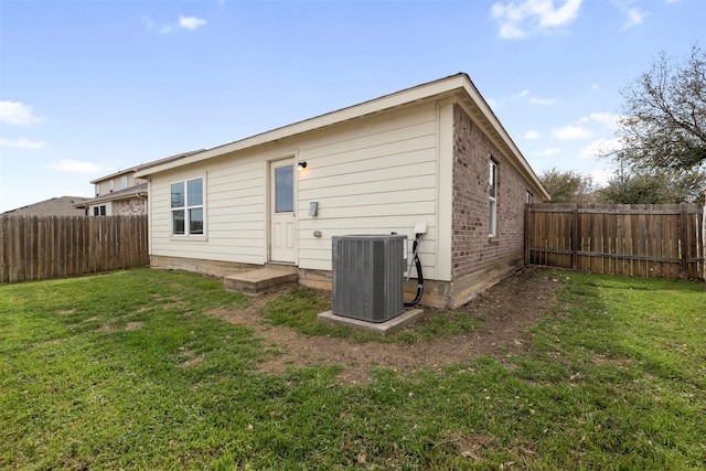 rear view of house featuring central air condition unit, a lawn, and a fenced backyard