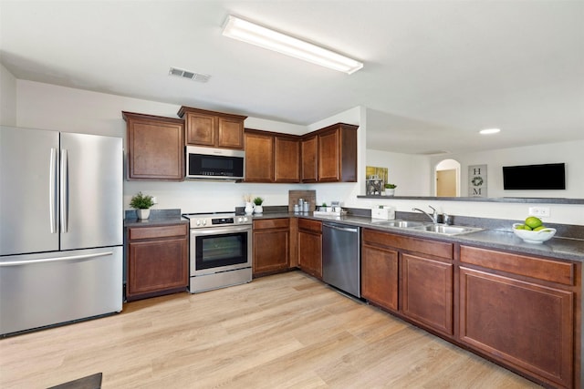 kitchen with visible vents, a sink, stainless steel appliances, dark countertops, and light wood-type flooring