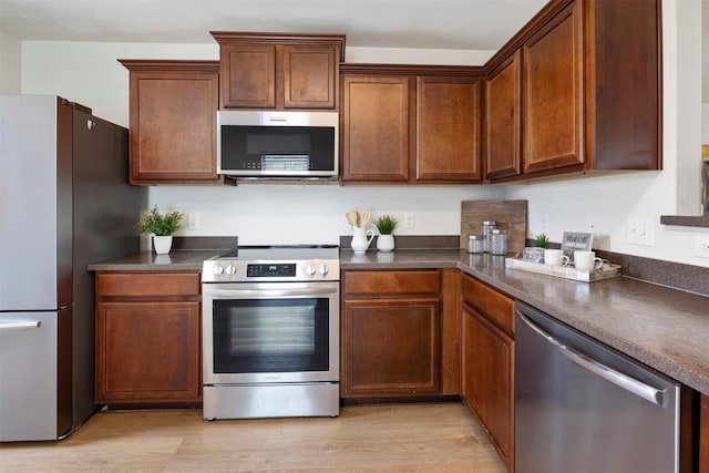 kitchen with dark countertops, appliances with stainless steel finishes, and light wood-style flooring