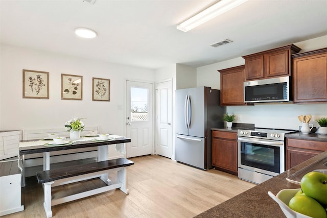 kitchen with light wood-style floors, stainless steel appliances, dark countertops, and visible vents