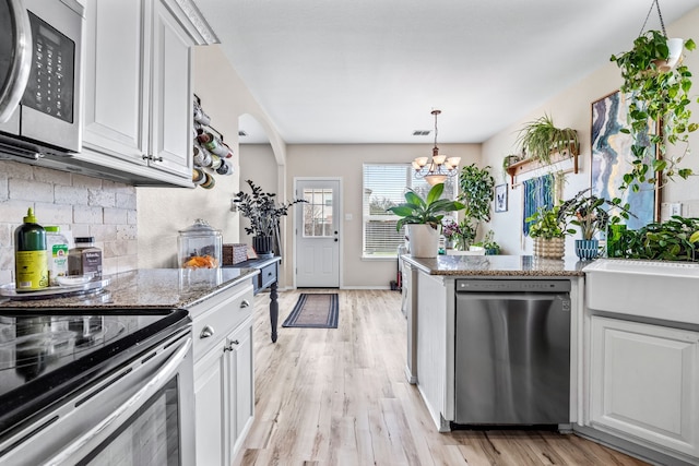 kitchen with light wood-style floors, stainless steel appliances, backsplash, and an inviting chandelier