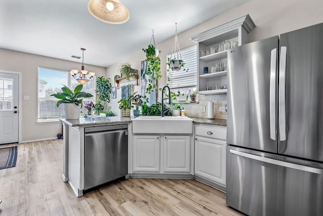 kitchen featuring light wood finished floors, open shelves, a peninsula, a sink, and appliances with stainless steel finishes