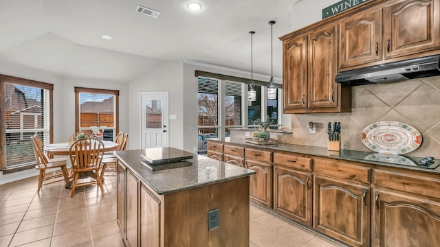 kitchen with visible vents, a kitchen island, under cabinet range hood, light tile patterned floors, and dark stone countertops