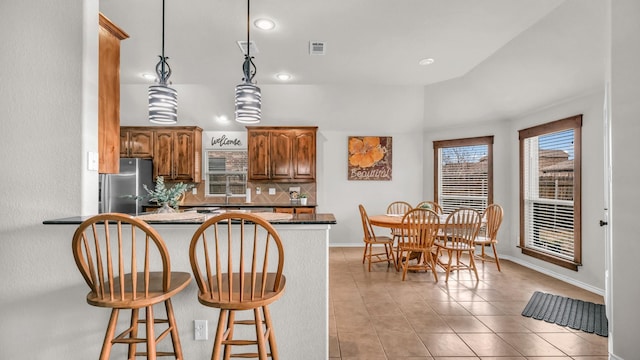 kitchen with a breakfast bar area, light tile patterned floors, brown cabinetry, freestanding refrigerator, and tasteful backsplash