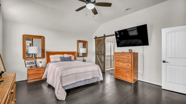 bedroom with a barn door, visible vents, dark wood finished floors, and vaulted ceiling