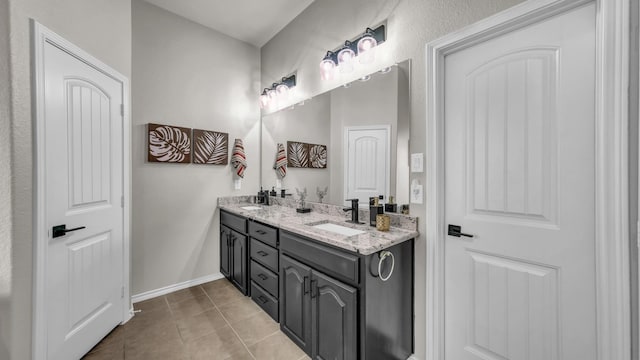 full bath featuring a sink, baseboards, double vanity, and tile patterned flooring