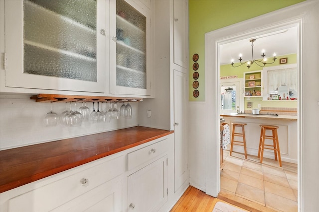 bar with wainscoting, an inviting chandelier, pendant lighting, and a bar