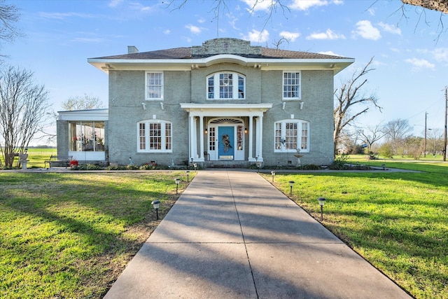 view of front facade with a chimney, a front yard, and brick siding