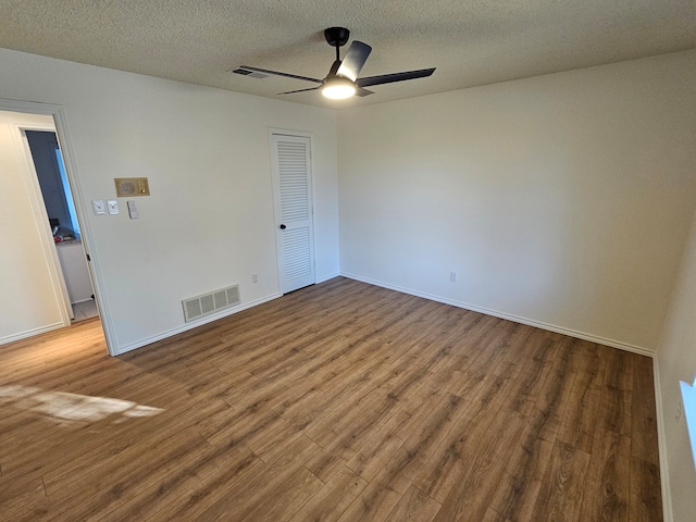 empty room featuring visible vents, a textured ceiling, ceiling fan, and wood finished floors