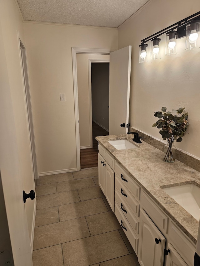 full bathroom featuring tile patterned floors, a sink, a textured ceiling, double vanity, and baseboards