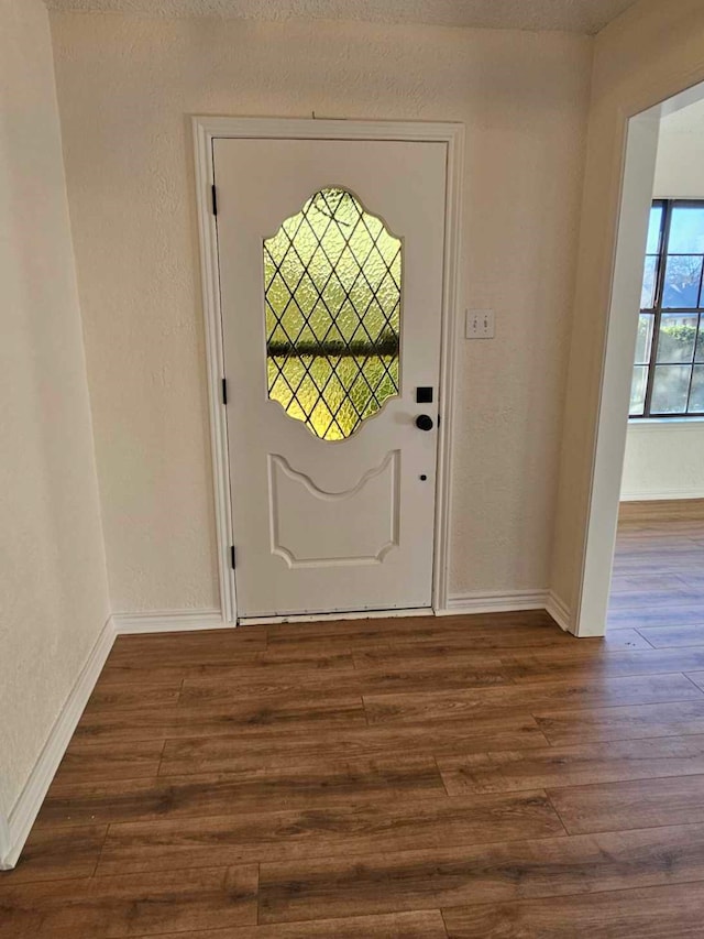 foyer featuring dark wood-type flooring, a textured wall, and baseboards