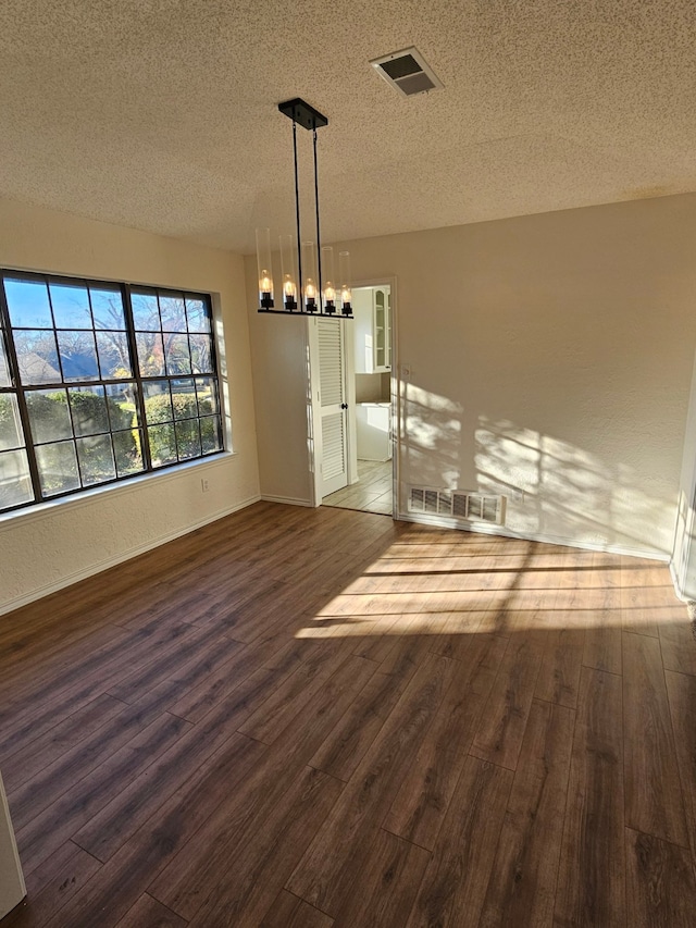 unfurnished room featuring visible vents, a textured ceiling, an inviting chandelier, and wood finished floors