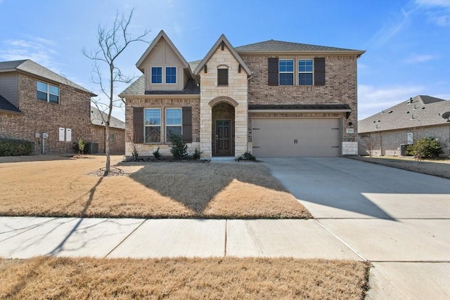 view of front of property featuring an attached garage, central AC, concrete driveway, stone siding, and brick siding