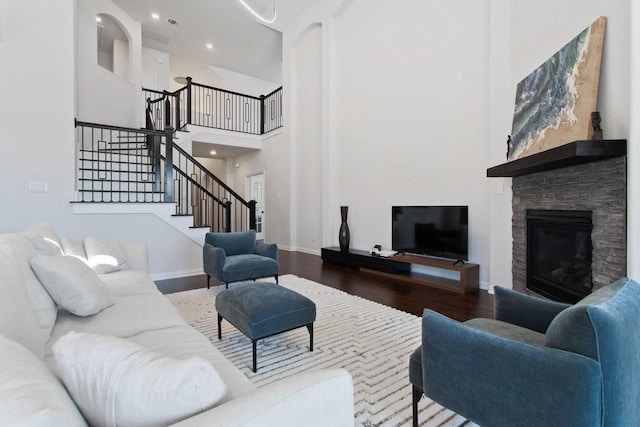 living room featuring baseboards, stairway, a fireplace, a high ceiling, and wood finished floors