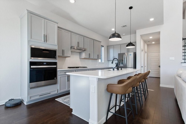 kitchen with gray cabinetry, tasteful backsplash, dark wood finished floors, appliances with stainless steel finishes, and light countertops