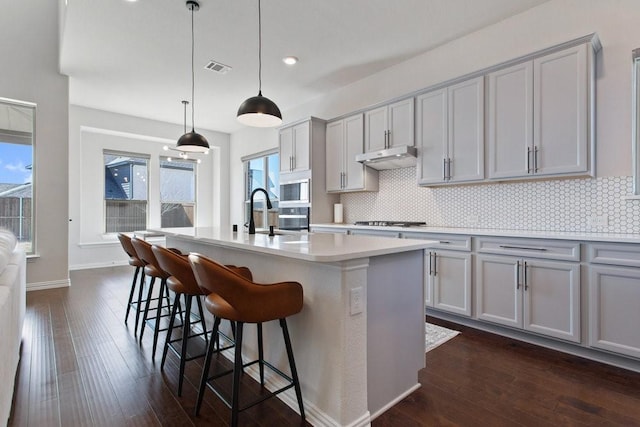 kitchen featuring white microwave, gray cabinets, stainless steel gas cooktop, and tasteful backsplash