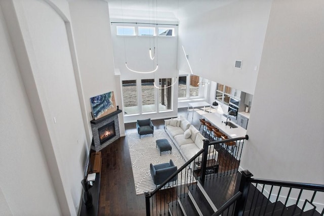 living room featuring visible vents, baseboards, a high ceiling, wood finished floors, and a glass covered fireplace