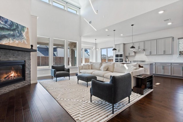 living area featuring visible vents, baseboards, recessed lighting, dark wood-style flooring, and a stone fireplace