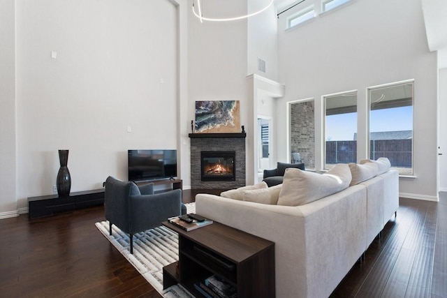 living room featuring visible vents, baseboards, dark wood-type flooring, and a stone fireplace