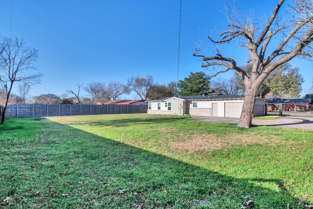 view of yard featuring concrete driveway, fence, and a garage