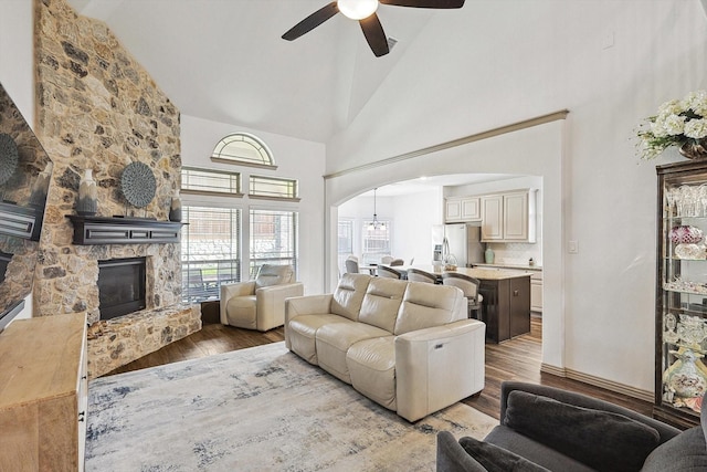 living area with ceiling fan, a stone fireplace, wood finished floors, arched walkways, and high vaulted ceiling