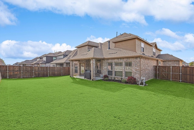 rear view of house with brick siding, roof with shingles, a lawn, a fenced backyard, and a patio area