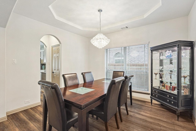 dining area featuring dark wood-style floors, a notable chandelier, and a raised ceiling