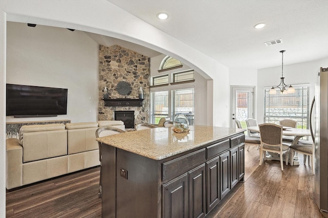 kitchen with visible vents, dark wood finished floors, pendant lighting, a stone fireplace, and freestanding refrigerator