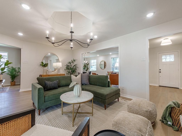 living area featuring light wood finished floors, baseboards, a tray ceiling, recessed lighting, and a notable chandelier