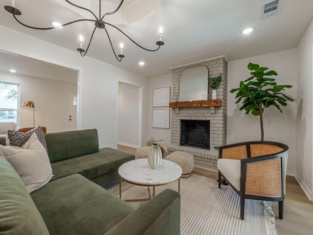 living room with visible vents, recessed lighting, light wood-style floors, a brick fireplace, and a chandelier