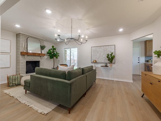 living room featuring baseboards, a brick fireplace, an inviting chandelier, and light wood finished floors