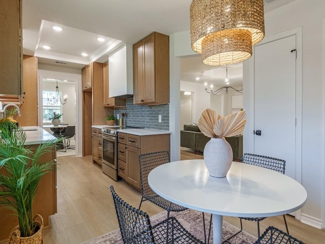 kitchen with wall chimney range hood, a chandelier, decorative backsplash, stainless steel electric range, and a sink