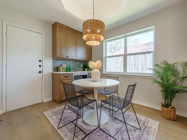 dining room with baseboards, a raised ceiling, an inviting chandelier, and light wood-style flooring