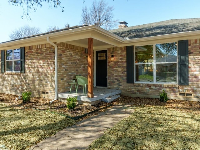 property entrance with brick siding, crawl space, a porch, and a chimney