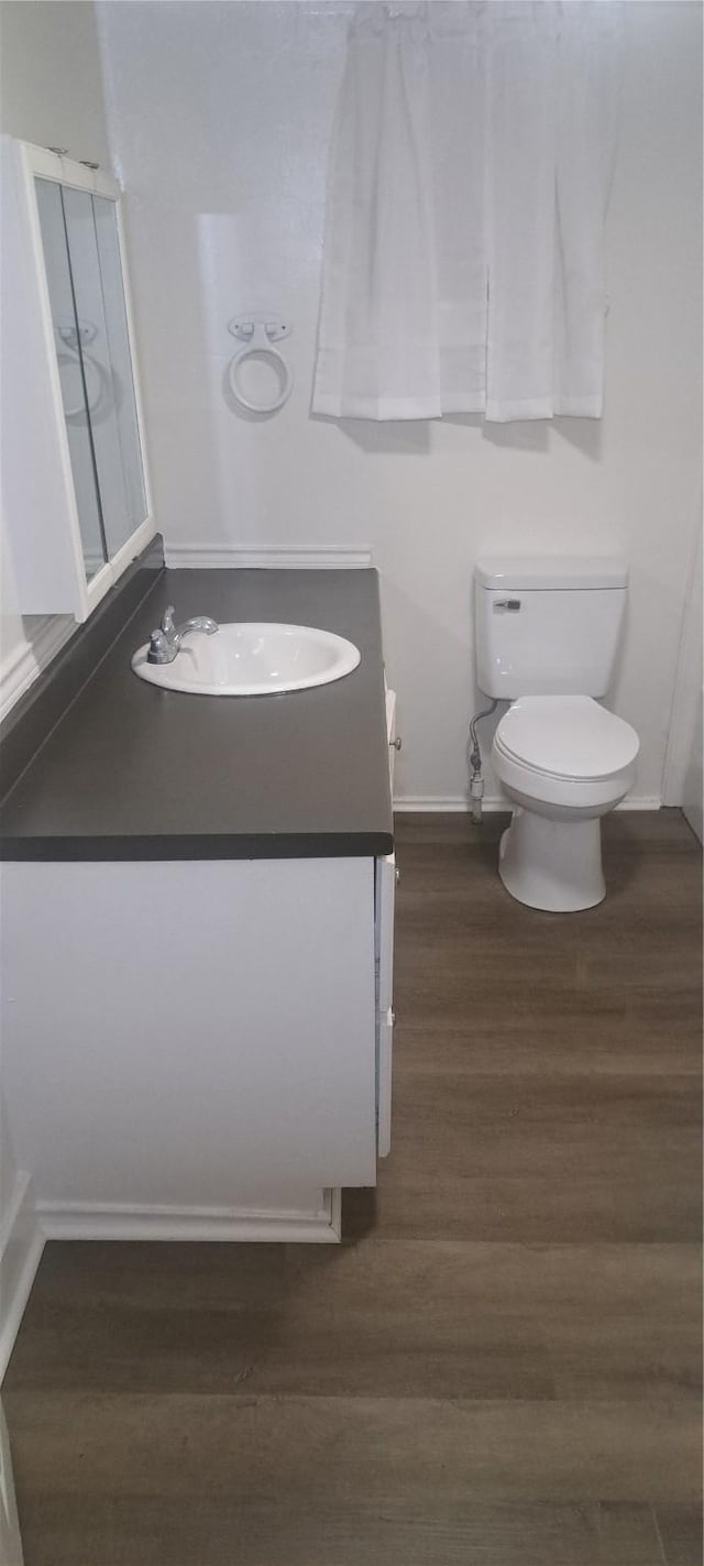 bathroom with baseboards, toilet, wood finished floors, and vanity