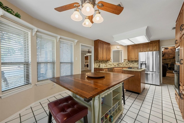 kitchen with ceiling fan, stainless steel appliances, light tile patterned flooring, and a center island