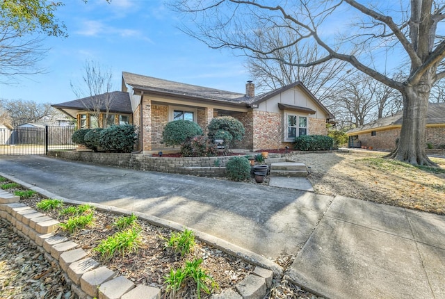 view of front of home with driveway, a gate, fence, brick siding, and a chimney