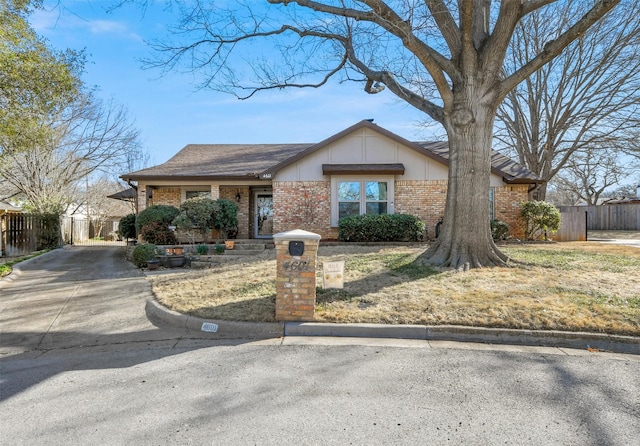 view of front of house featuring brick siding, driveway, and fence