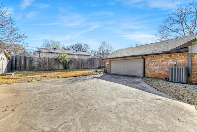 view of side of home featuring brick siding, fence, concrete driveway, central AC, and a garage