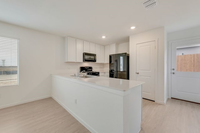 kitchen featuring visible vents, light countertops, light wood-style flooring, a peninsula, and black appliances