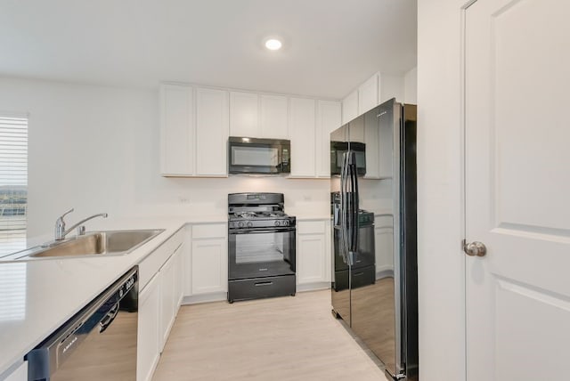 kitchen featuring a sink, black appliances, white cabinets, light countertops, and light wood-style floors