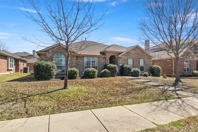 single story home with brick siding, a chimney, a front lawn, and roof with shingles