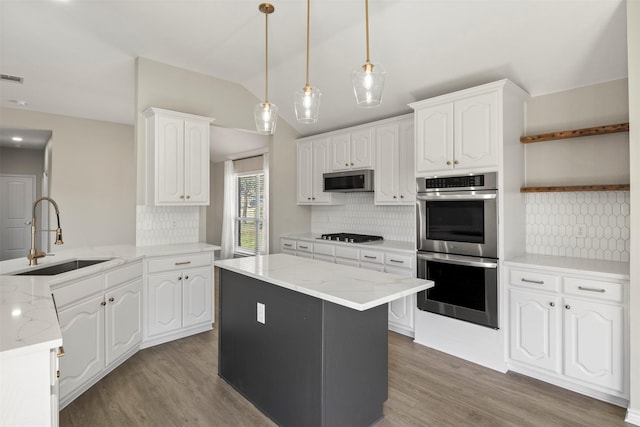 kitchen featuring vaulted ceiling, light wood-style flooring, appliances with stainless steel finishes, white cabinets, and a sink