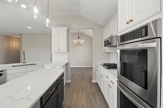 kitchen with a chandelier, vaulted ceiling, appliances with stainless steel finishes, white cabinets, and a sink