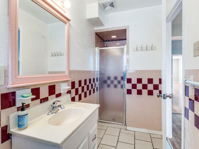 bathroom with tile patterned floors, visible vents, a stall shower, tile walls, and vanity