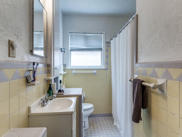 bathroom featuring vanity, curtained shower, tile walls, toilet, and a textured wall