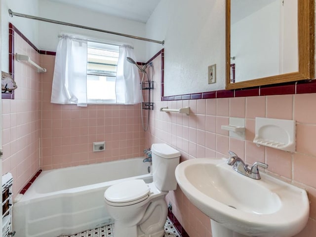 bathroom featuring a wainscoted wall, toilet, a sink, tile walls, and shower / bath combination