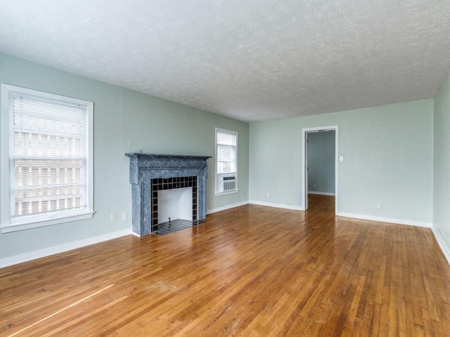 unfurnished living room featuring baseboards, wood-type flooring, a textured ceiling, and a tiled fireplace